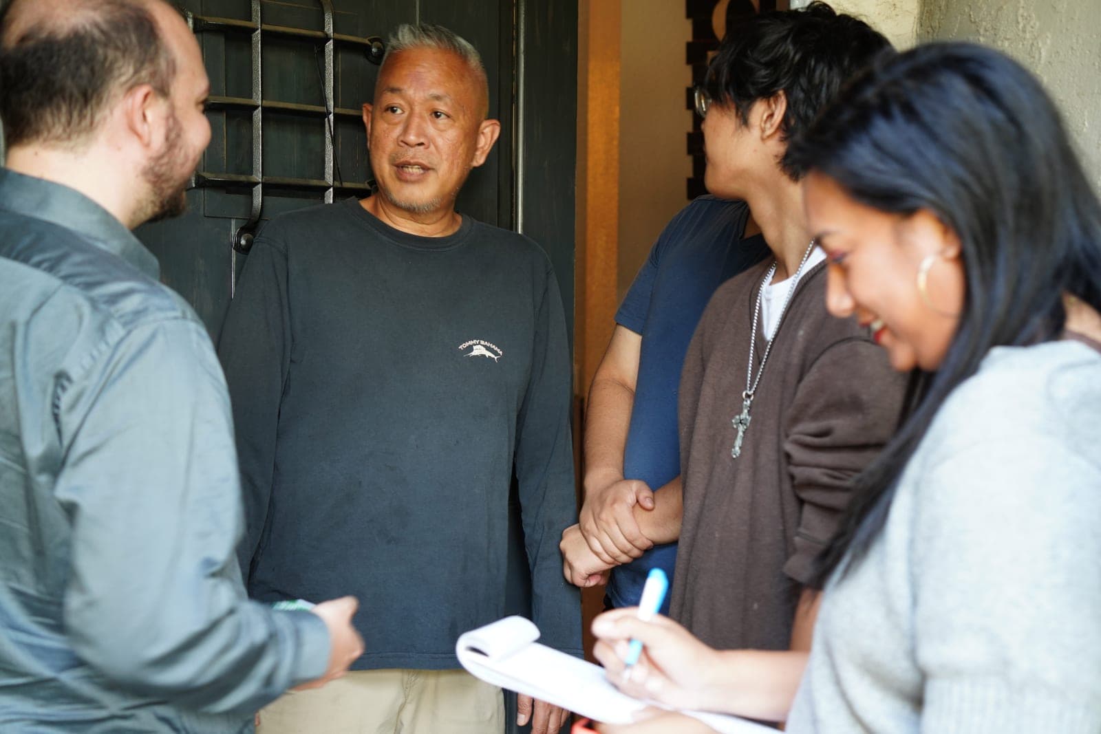 Justin talking with a family in their doorway while a volunteer takes notes