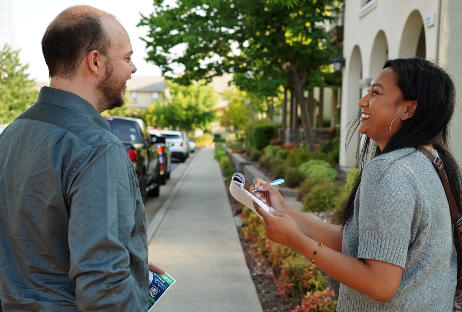 Justin laughing on a sidewalk with a volunteer holding a notepad