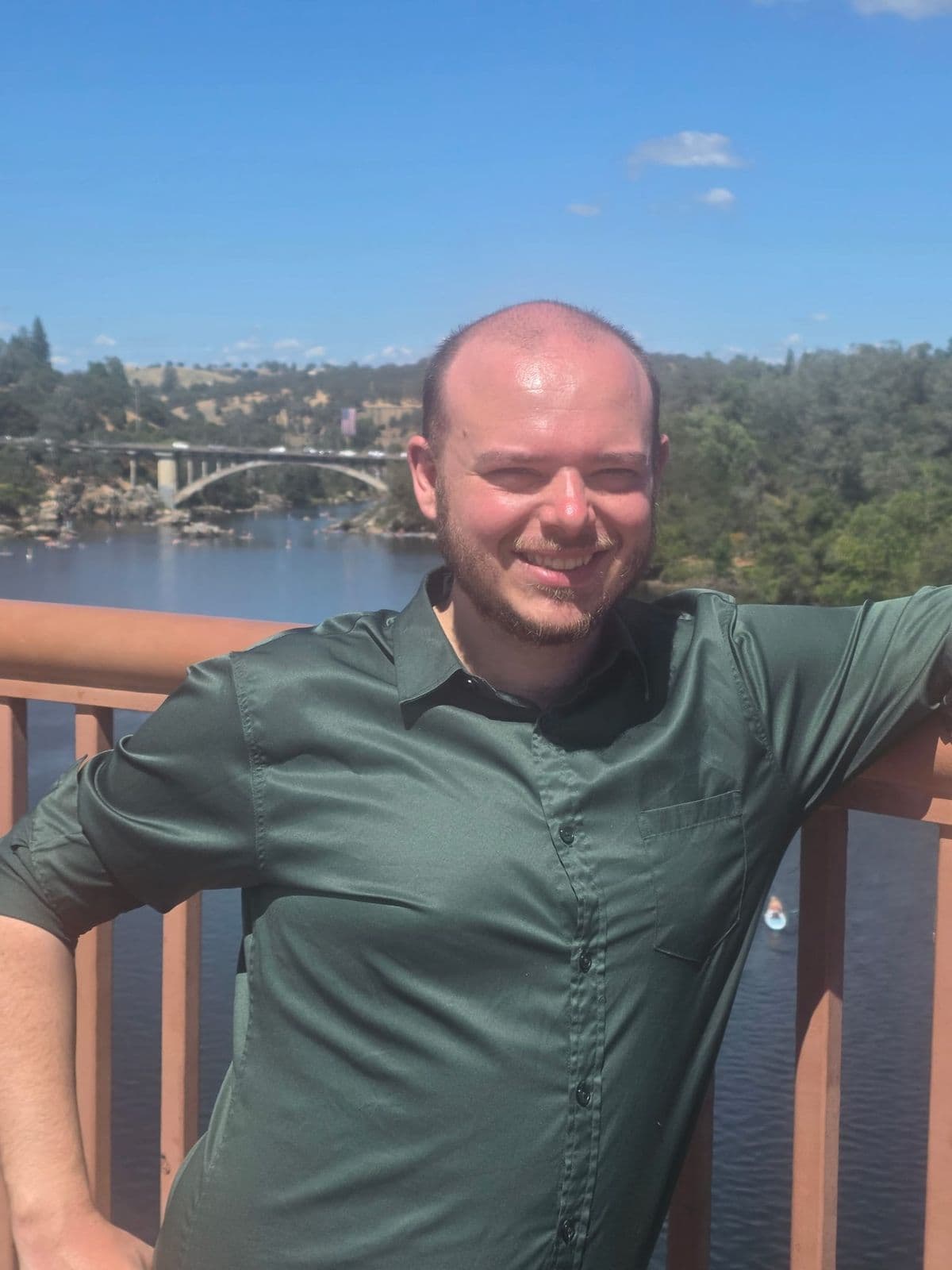 Justin smiling on a deck above Lake Natoma with a bridge behind him