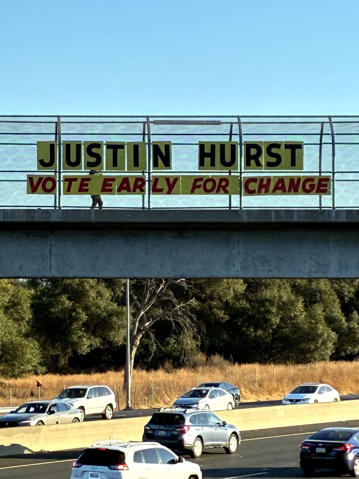 A Justin Hurst Vote Early for Change banner hanging on a freeway overpass
